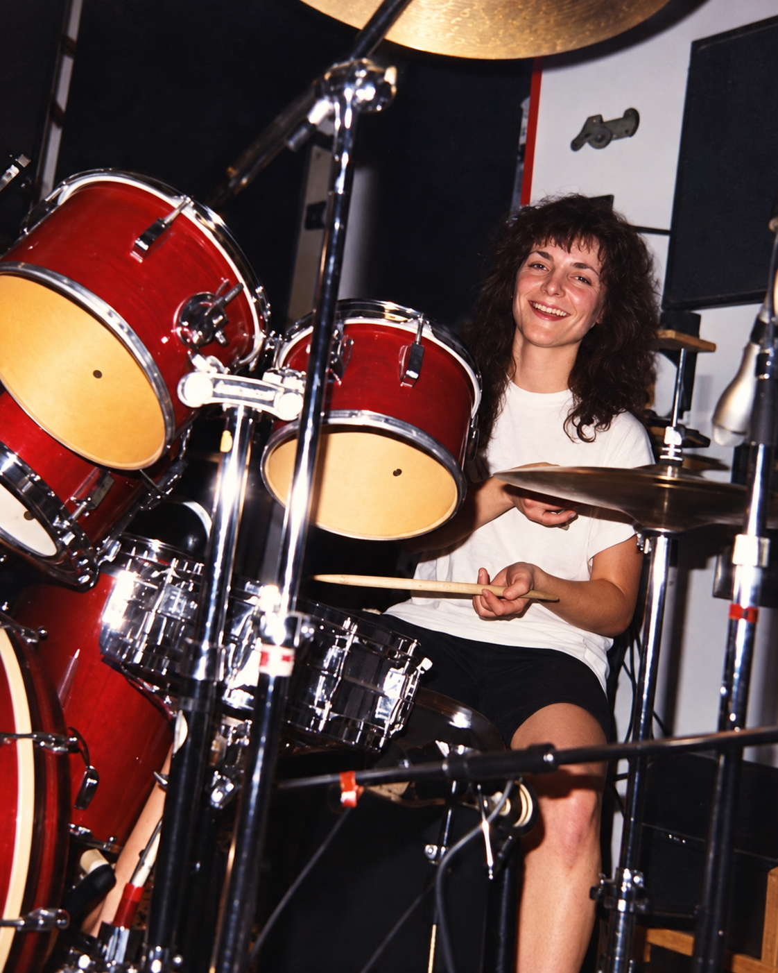 Mary seated behind a red drum kit holding drumsticks